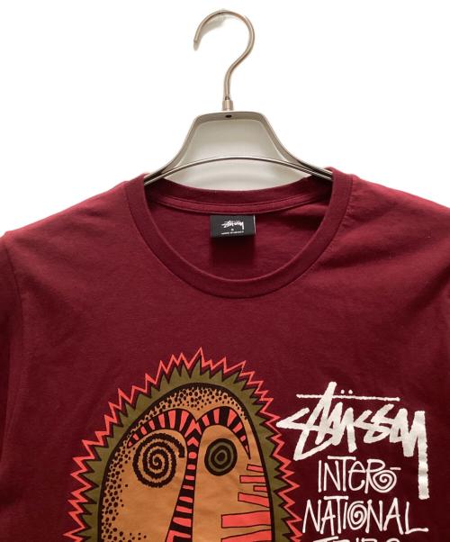 stussy（ステューシー）stussy (ステューシー) トライバルマスクプリントTシャツ パープル サイズ:Sの古着・服飾アイテム