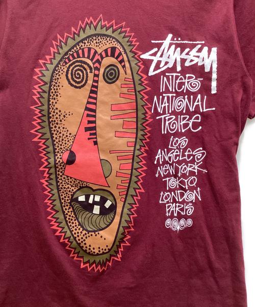 stussy（ステューシー）stussy (ステューシー) トライバルマスクプリントTシャツ パープル サイズ:Sの古着・服飾アイテム